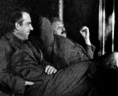 Two men sitting, looking relaxed. A dark-haired Bohr is talking while Einstein looks skeptical.