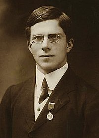 Sepia toned photo of young man wearing a suit, a medal, and wire-rimmed eyeglasses